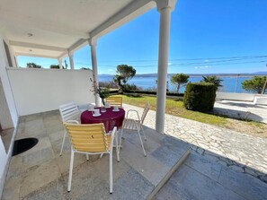 A covered outdoor seating area with a table and chairs, a view of a body of water, and a stone pathway. - Apartment Luky 3 (Dramalj)