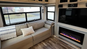 A cozy RV interior with a sectional sofa, a fireplace, and a large window offering a view of the outside. - Luxury 1-bedroom RV with AC, WiFi in charming Bonavista (Bonavista)