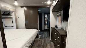 A compact RV interior with a bed, kitchenette, and a small bathroom. - Luxury 1-bedroom RV with AC, WiFi in charming Bonavista (Bonavista)
