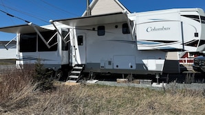 A Columbus RV with a covered front area and a chimney, parked in a grassy area with a clear blue sky. - Luxury 1-bedroom RV with AC, WiFi in charming Bonavista (Bonavista)