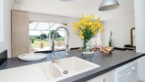 Eine moderne Küche mit einem großen Spülbecken, zwei Pendelleuchten und einem Blumenstrauß mit gelben Blumen auf der Arbeitsplatte.