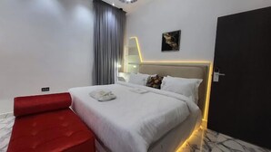 A modern hotel room with a bed, a red sofa, a painting on the wall, and a door. - Elite Palace Hotel  (Abuja)