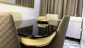 A dining area with a black table, beige cushioned chairs, a white cabinet, and a mirror on the wall. - Elite Palace Hotel  (Abuja)