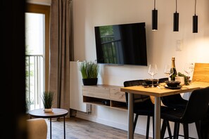 A modern dining area with a wooden table, black chairs, a TV mounted on the wall, and a potted plant. - Nuevo Studiot Klimatyzacja Balkon Smart TV (Bydgoszcz)