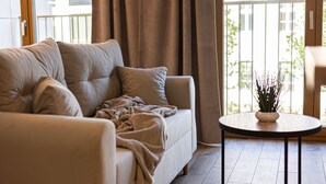 Ein Wohnzimmer mit einem beigen Sofa, einem runden Tisch und Blick auf einen Balkon mit Pflanzen.