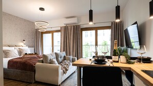 Ein modernes Hotelzimmer mit Bett, einer Couch, einem Esstisch mit Stuhl, einem Fernseher und Balkonblick.