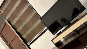 A room with a flat-screen TV on a wooden stand, a brown door, and a white wall. - Large and comfortable room (Downtown) (Cochabamba)