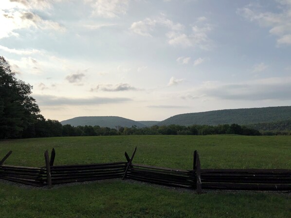 Ein grasbewachsenes Feld mit einem Holzzaun und einer hügeligen Landschaft im Hintergrund.