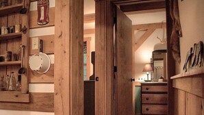 Un interior rústico con paredes de madera, una puerta que da a otra habitación y un estante con diversos objetos.