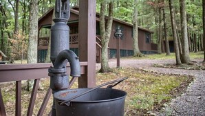 Un entorno rústico al aire libre con una estructura de madera, una bomba de agua de metal y una olla grande.