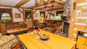 Una sala de estar acogedora con chimenea, vigas de madera y un comedor con una mesa dispuesta para una comida.
