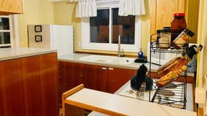 A compact kitchen with wooden cabinets, a white countertop, a window with curtains, and a metal rack holding kitchen utensils.