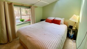 A bedroom with a bed, a nightstand, a lamp, a window with curtains, and a skylight.