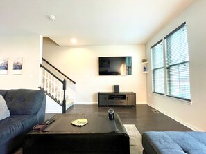 Un salon avec un canapé, une table basse, un téléviseur et un escalier.