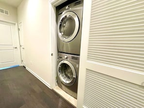 Une buanderie équipée de deux machines à laver à chargement frontal superposées, d’une porte et d’une bouche d’aération au mur.
