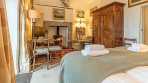 A cozy room with a fireplace, a bed with towels, a wooden wardrobe, and a bookshelf. - 2-Bryn-Tirion | Charming Traditional Cottage with Stunning Sea Views (Pwllheli)