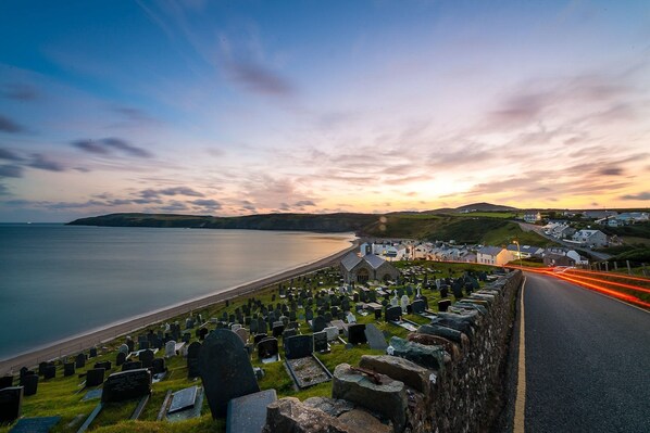 A coastal cemetery with headstones, a road, and a sunset in the background.