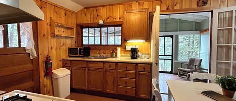 Une cuisine rustique aménagée dans une cabane en bois, avec une cuisinière à gaz, un four à micro-ondes, un évier et des placards en bois.