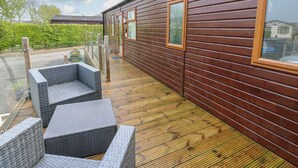 Een houten blokhut met terras, rieten meubilair en een glazen reling.