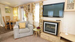 Een gezellige woonkamer met een bank, een televisie, een open haard en een eethoek met stoelen en een tafel.
