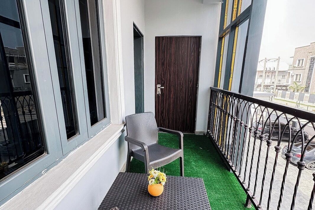 Un balcón con una silla, una mesita con un florero y una puerta.