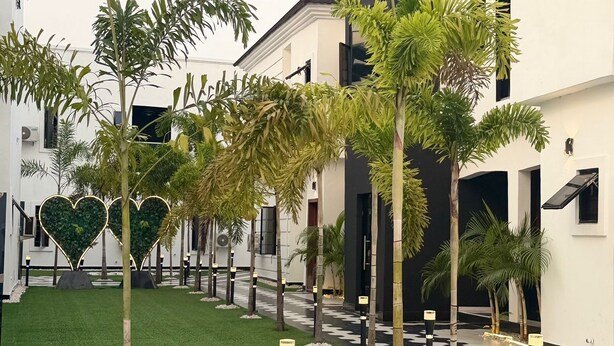 A courtyard with a geometric tile floor, palm trees, and a building with a dark roof and white walls.