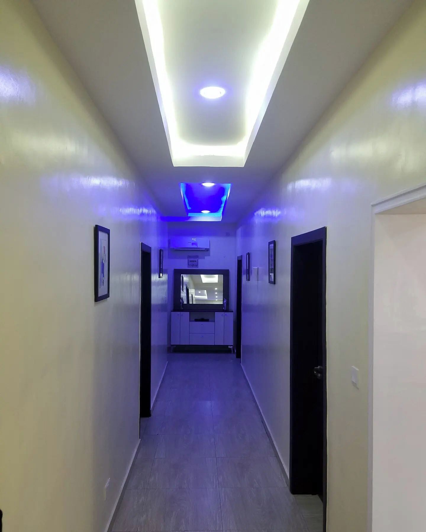 Un pasillo con un diseño moderno en el techo, que incluye iluminación empotrada y un elemento de luz central.