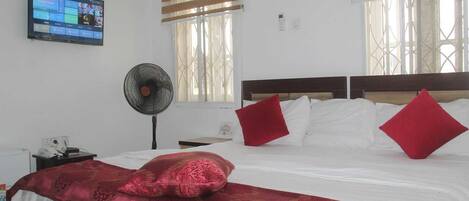 Habitación de hotel con cama, televisor montado en la pared, ventilador y ventana con persianas.