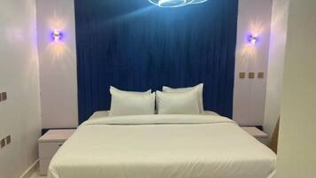 A modern hotel room with a large bed, two bedside tables, and a blue curtain backdrop.