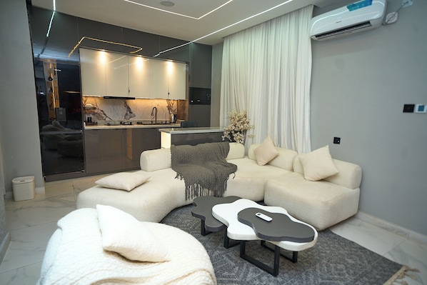 A modern living room with a sofa, a coffee table, and a kitchen area visible through a glass partition.