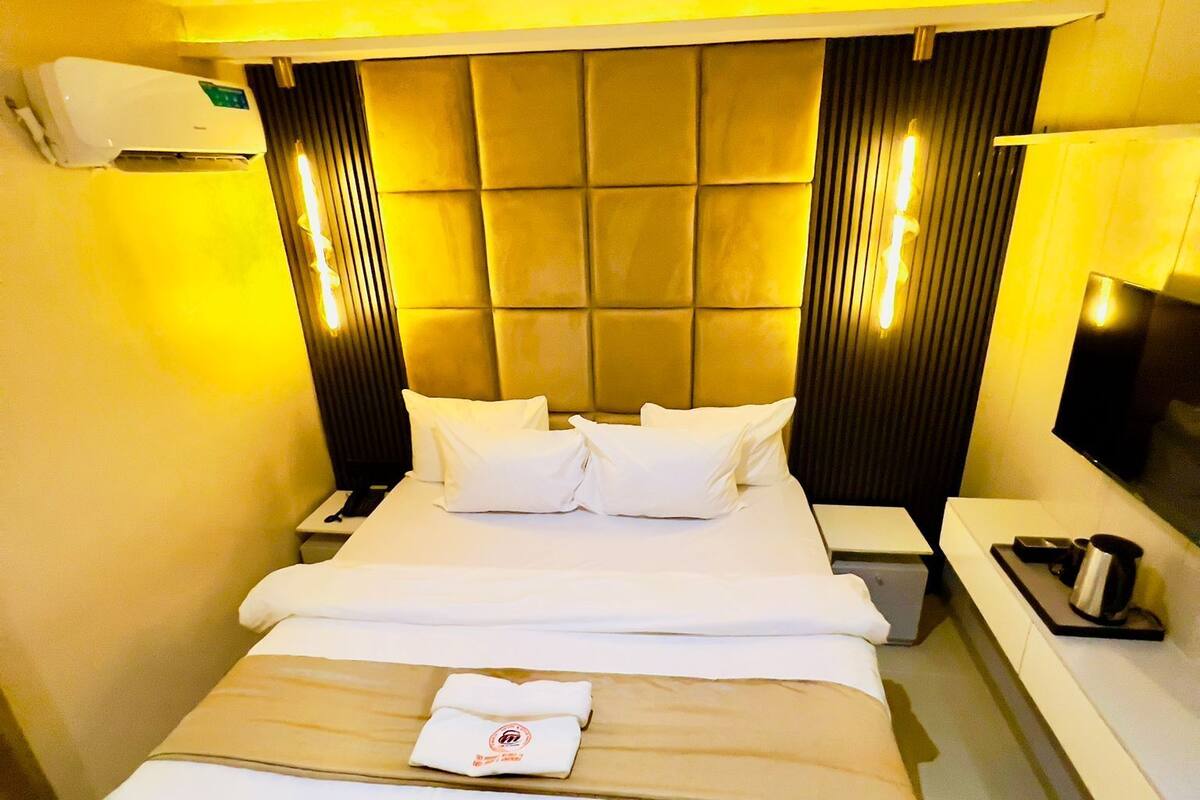 A hotel room with a large bed, bedside tables, a bedside lamp, and a wall-mounted air conditioner.