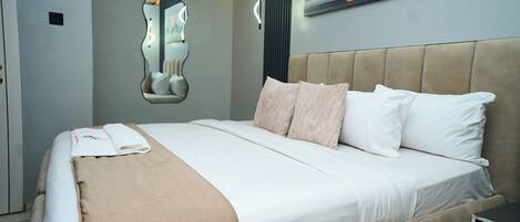 A neatly made bed with a beige headboard, a wall-mounted mirror, and a painting.