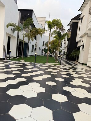 A modern building with a geometric black and white tiled floor, surrounded by greenery and white walls.