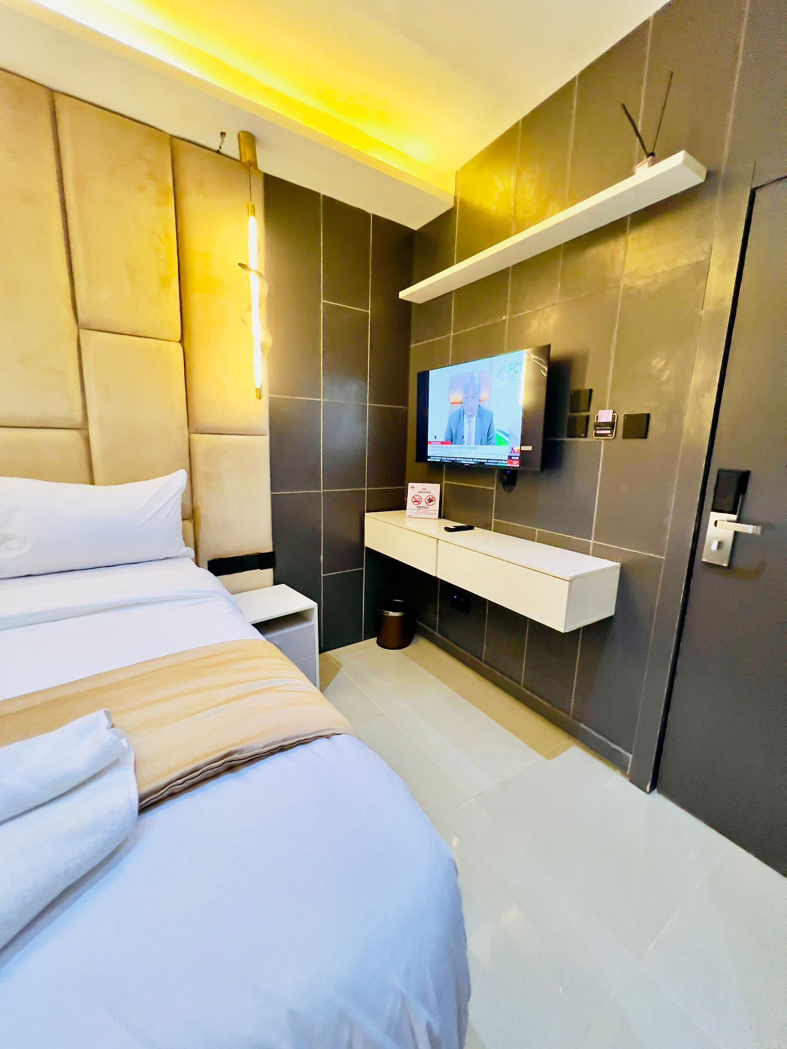 Een moderne hotelkamer met een groot bed, een aan de muur bevestigde televisie, een nachtkastje en een kleine prullenbak.