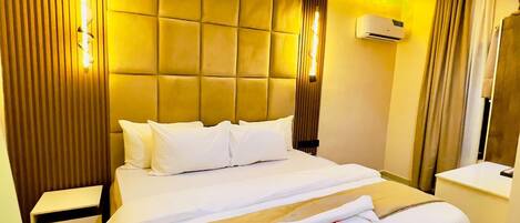 A hotel room with a large bed, a bedside table, an air conditioning unit, and a mirror.