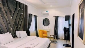 A modern hotel room with a large bed, a yellow armchair, a small table, and a mirror.