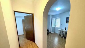 A hallway with wooden flooring leading to a room with a door, a dining area with a table and chairs, and a ceiling light. - Villa Julie (Jadranovo)