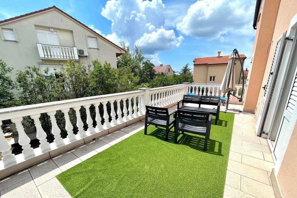 A balcony with artificial grass, a white balustrade, and a table with chairs.