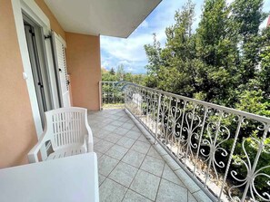 Un balcone con ringhiera in metallo bianco, una sedia in plastica bianca e un tavolo bianco.