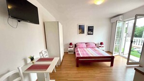 A bedroom with a bed, a TV, a desk with chairs, and a balcony with a view. - Villa Julie (Jadranovo)