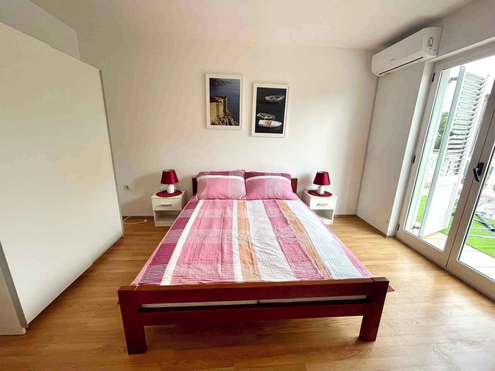 Een slaapkamer met een houten bed, twee nachtkastjes, een raam met uitzicht en twee aan de muur hangende foto's.