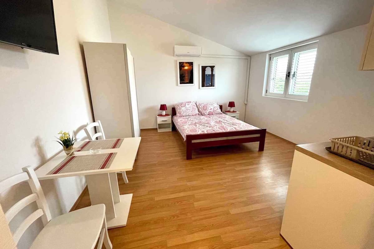 A bedroom with a bed, bedside tables, a desk, chairs, a TV, and a window.
