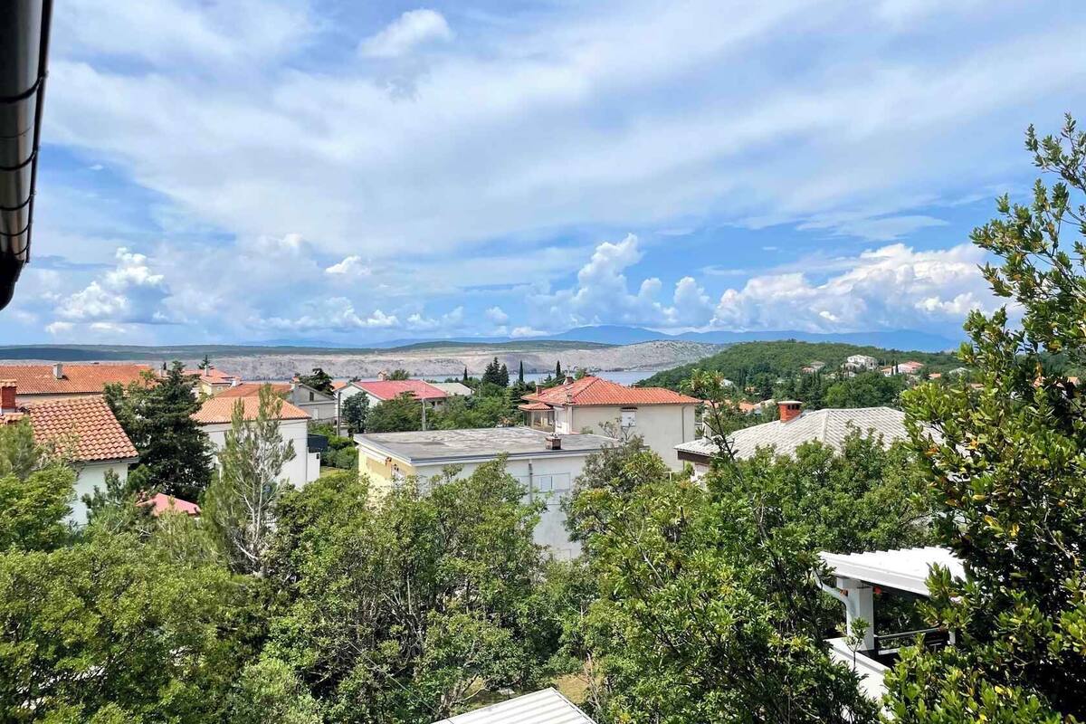A residential area with houses, trees, and a distant view of hills and mountains under a partly cloudy sky.