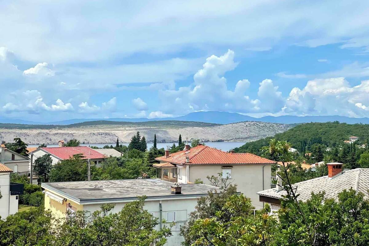 A residential area with houses featuring red-tiled roofs and a backdrop of mountains and a lake.