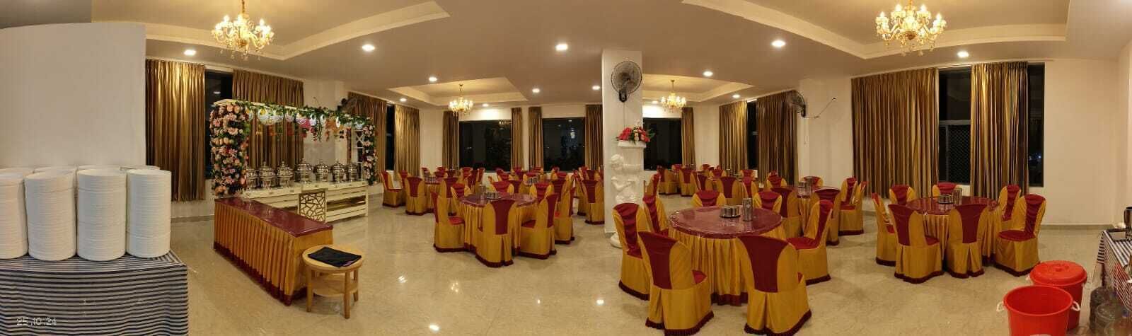 A banquet hall with round tables and chairs, a stage with floral decorations, and a chandelier.