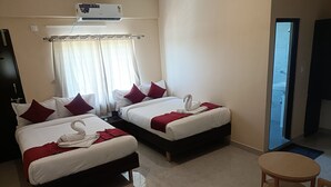 Habitación de hotel con dos camas, cada una con ropa de cama blanca y almohadas rojas, una manta roja y una toalla dispuesta en forma de cisne. En la esquina hay una pequeña mesa de madera y una silla.