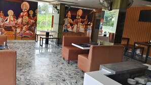 Un restaurante con pisos de mármol, asientos color naranja y murales de deidades.