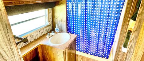 Une petite salle de bain avec un meuble-lavabo en bois, un évier, un lavabo jaune et un rideau de douche bleu.