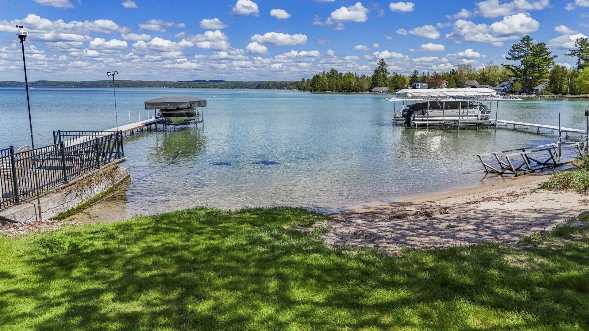 Un muelle sobre el lago con un bote cubierto, una playa de arena y una zona arbolada.