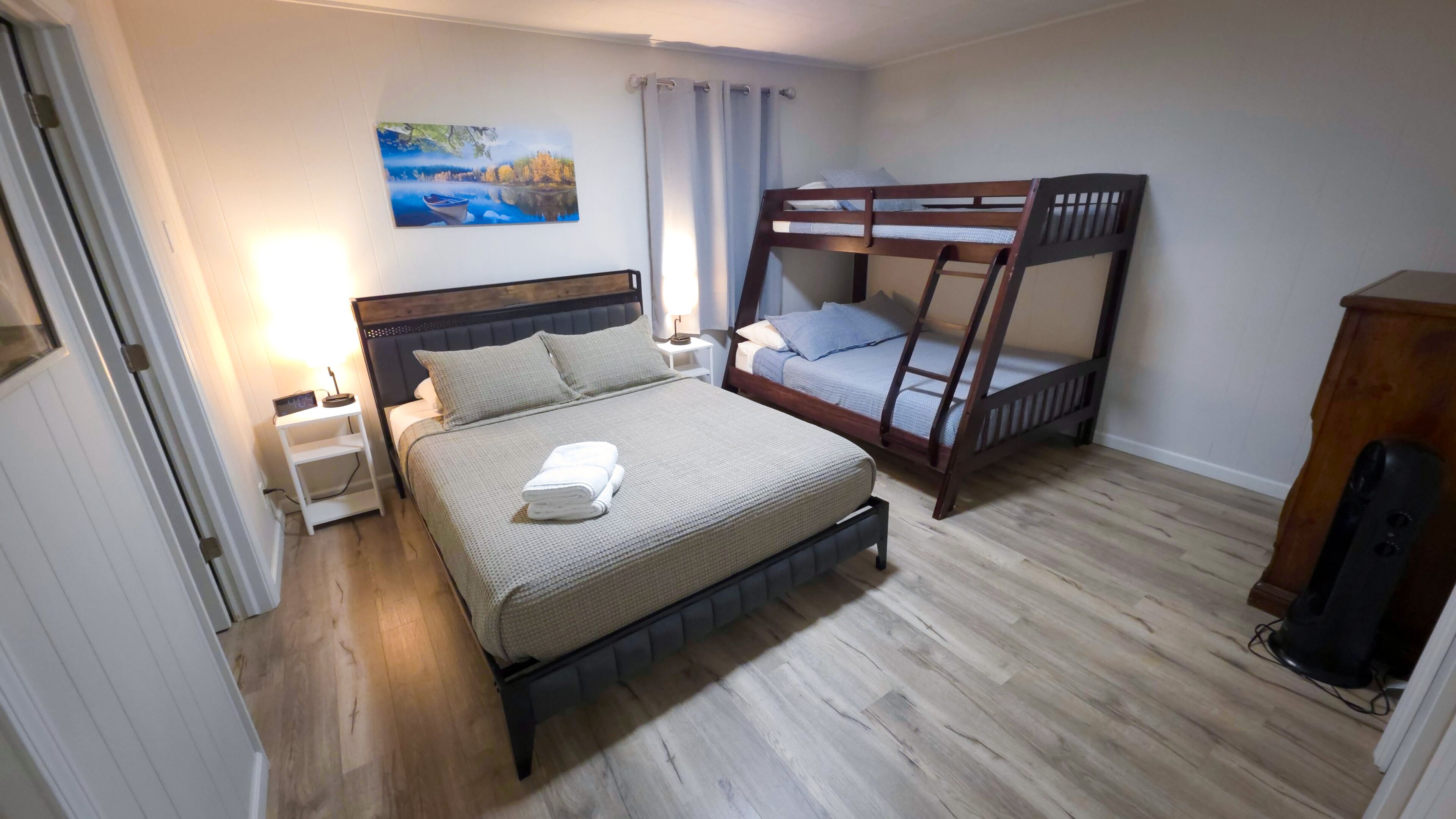 A bedroom with a bed, a bunk bed, a nightstand, a lamp, a painting, and a speaker.